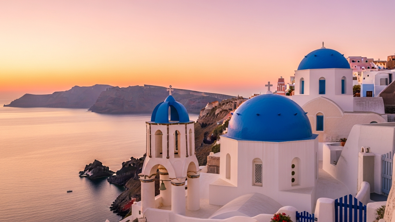 โบสถ์โดมสีน้ำเงินของ Santorini ยามเช้าตรู่ใน Oia ท้องฟ้าสีชมพูอ่อน บรรยากาศเงียบสงบ